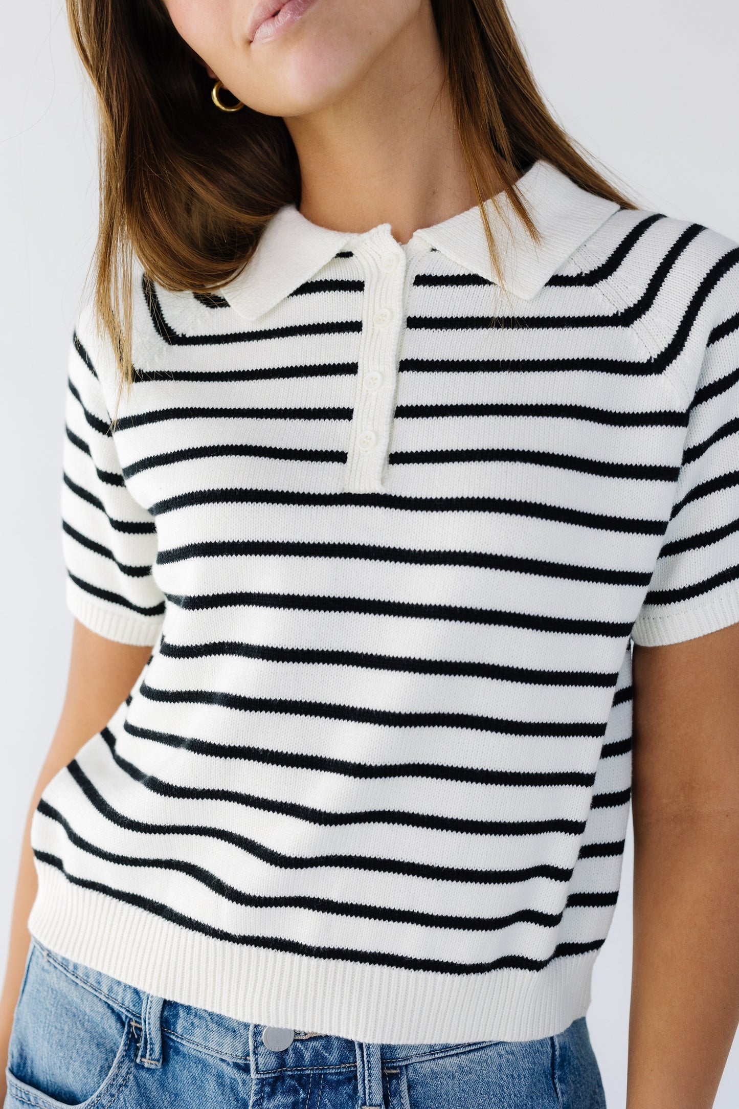 Close view of a woman wearing a a white and black stripe short sleeve sweater with a short button placket & a pointed collar.