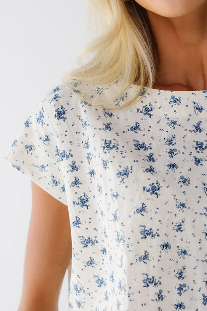 Close view of a woman wearing a cream and blue floral short sleeve top.