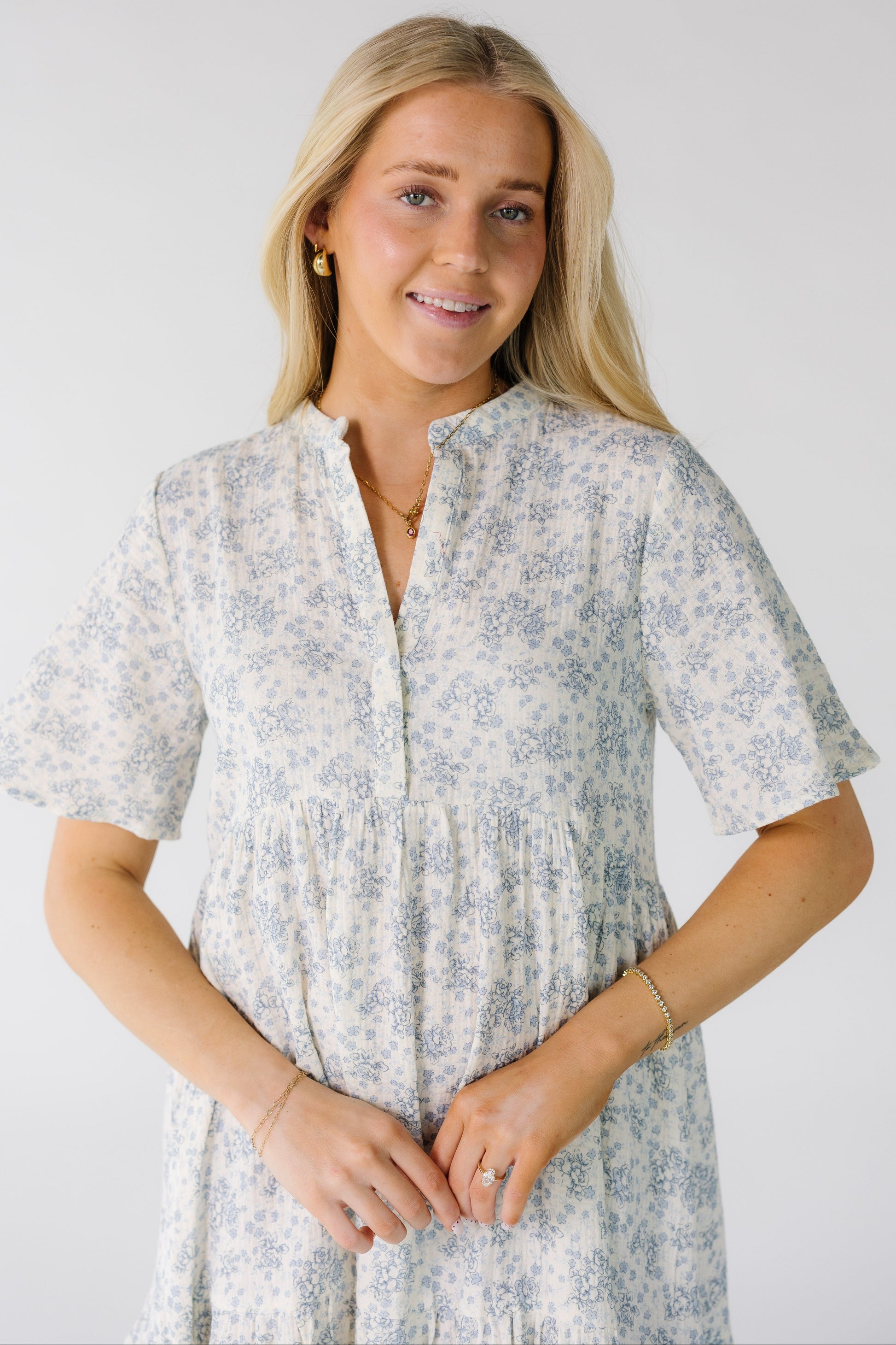 Close view of a woman wearing a modest white gauzy dress with blue floral print with a V-neckline short sleeves.
