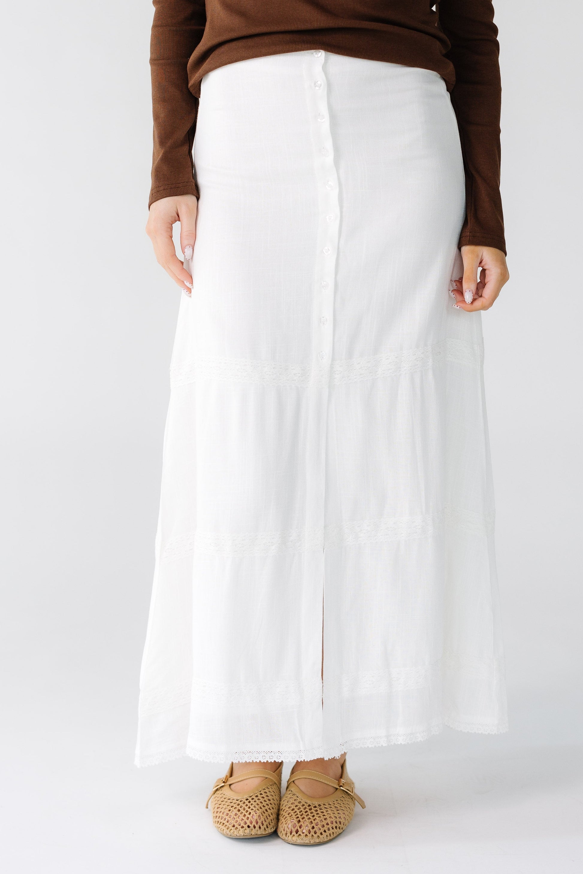 Woman wearing a modest  A-line button down midi skirt with a center front slit with 3 white lace stripes.