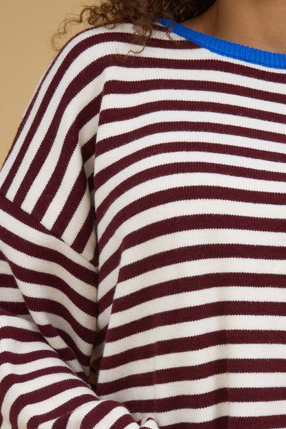 Close view of a young woman wearing a burgundy s& cream stripe sweater with a blue crew neckline.
