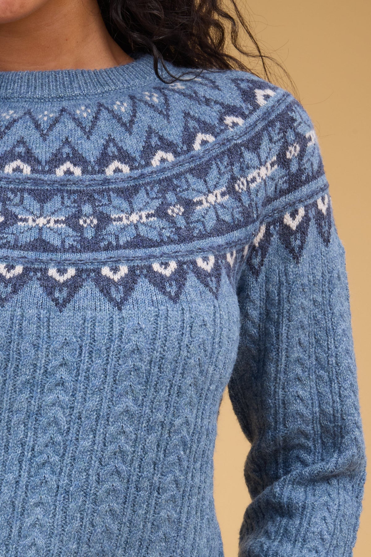 Close view of a woman wearing a blue cable knit sweater with a nordic pattern in navy, blue & white.