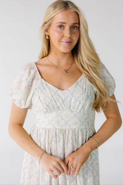 Close view of a woman wearing a white with blue floral dress with a sweetheart neckline with short puff sleeves.