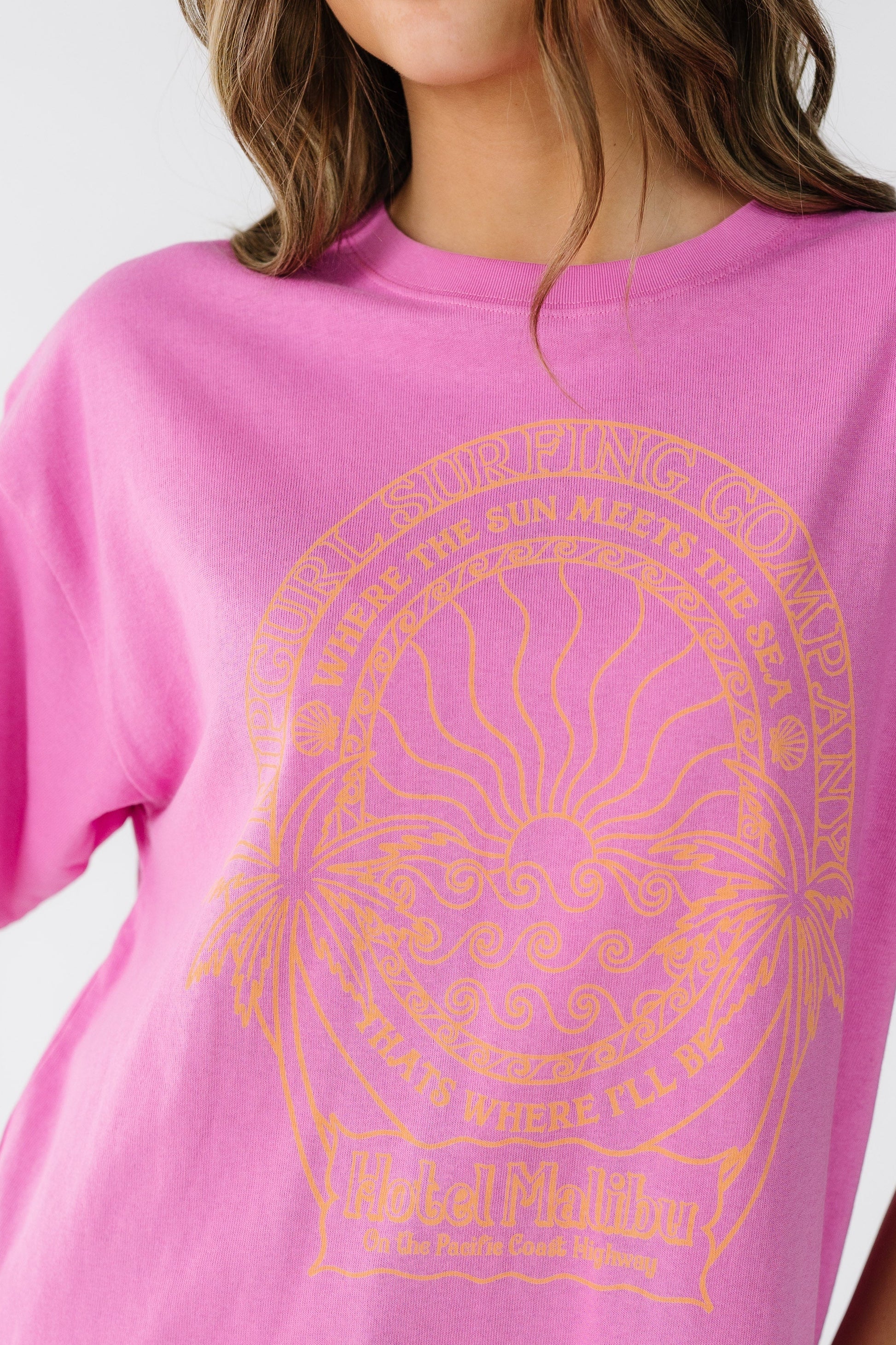 Close view of a young woman wearing a bright pink short sleeve tee with a crew neckline and a large orange graphic on the front.