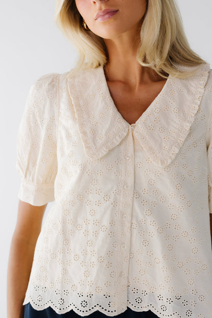 Close view of a woman wearing a fully lined all eyelet blouse in cream that buttons down the front and a V-neckline and ruffle edged lapels.