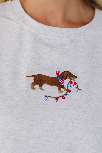 Close view of an embroidered dog & USA banner graphic on a heather grey short sleeve tee.