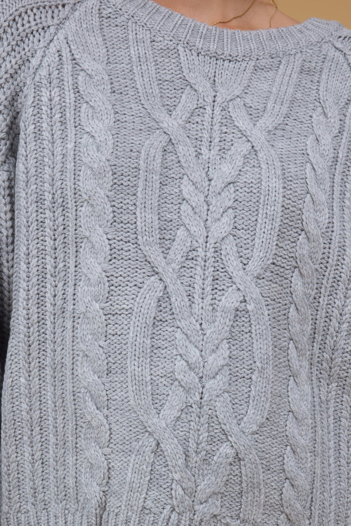 Close front view of a woman wearing a grey multi-cable knit sweater.