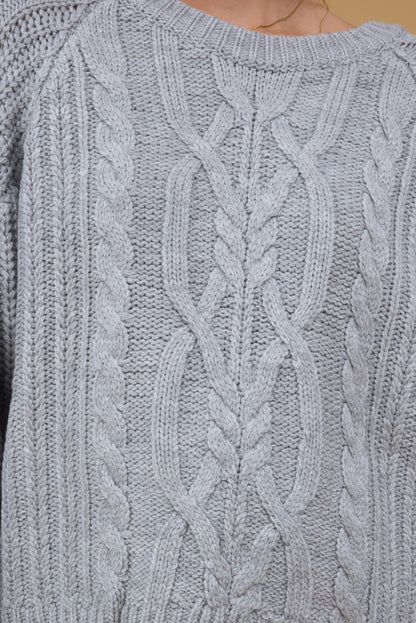 Close front view of a woman wearing a grey multi-cable knit sweater.