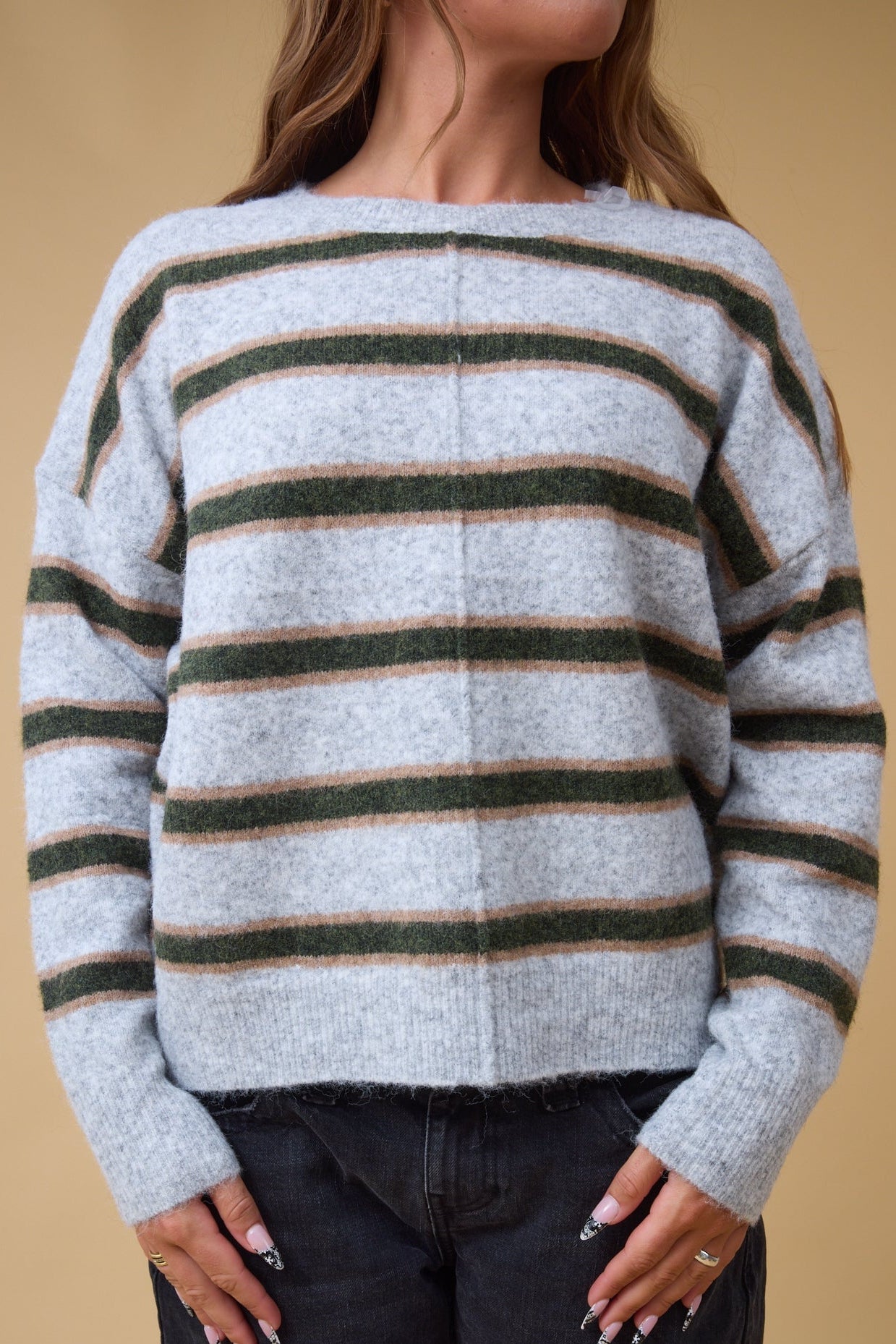 Close view of a woman wearing a loose fitting pullover sweater with a center deorative seam in grey, green & gold stripes.