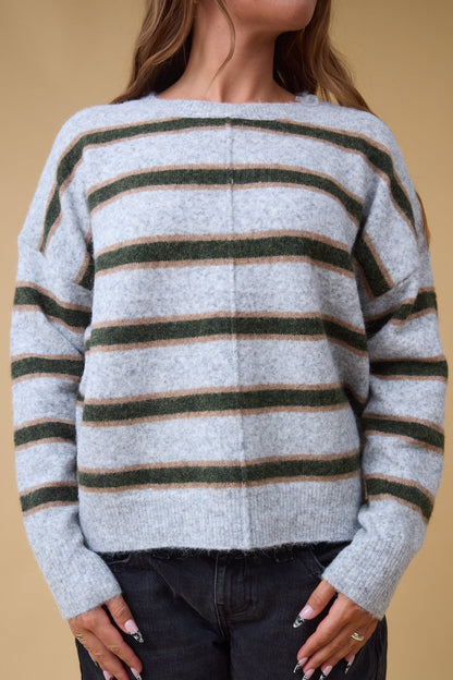 Close view of a woman wearing a loose fitting pullover sweater with a center deorative seam in grey, green & gold stripes.