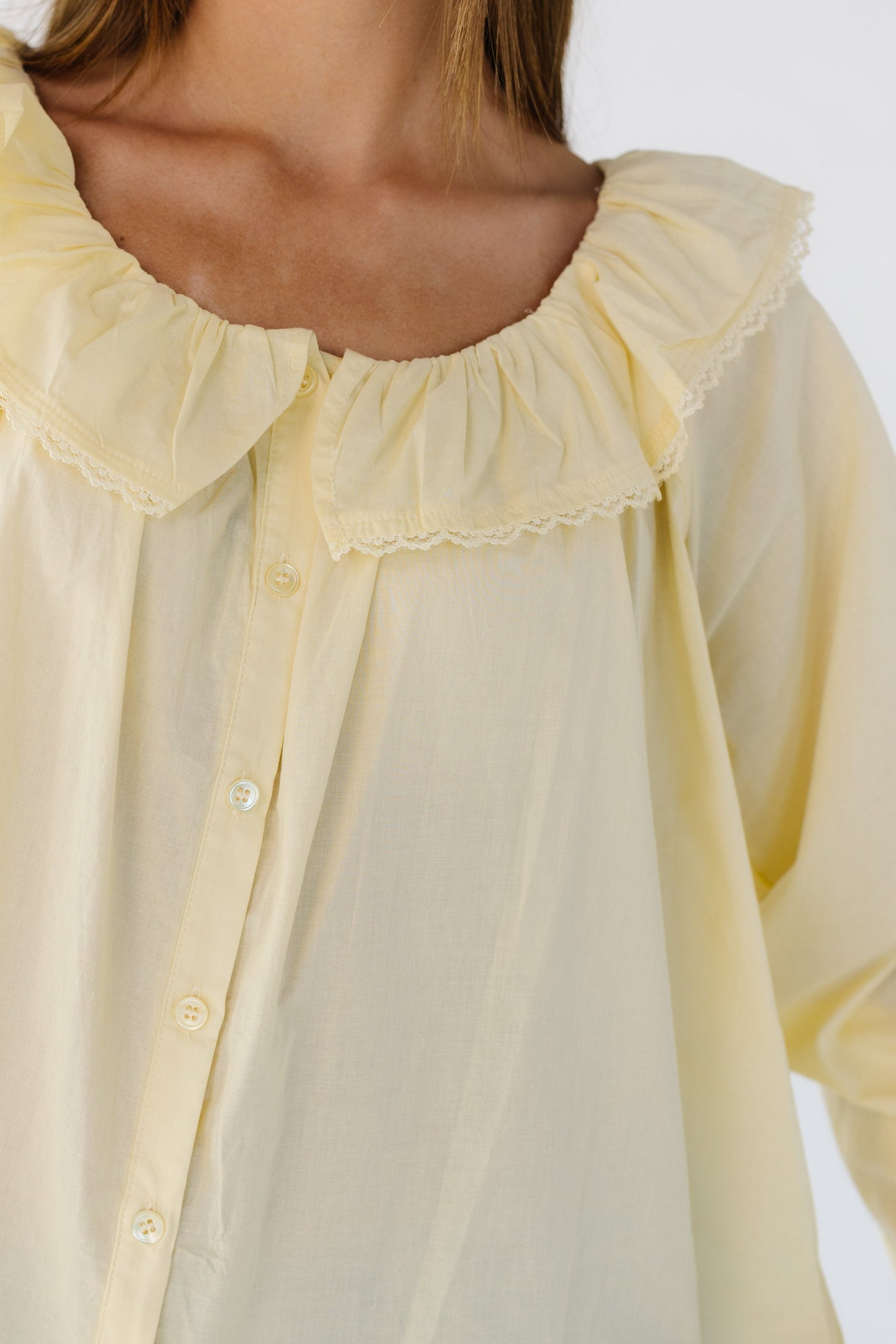 Close view of a woman wearing a yellow button down blouse with a lace trimmed ruffled collar.