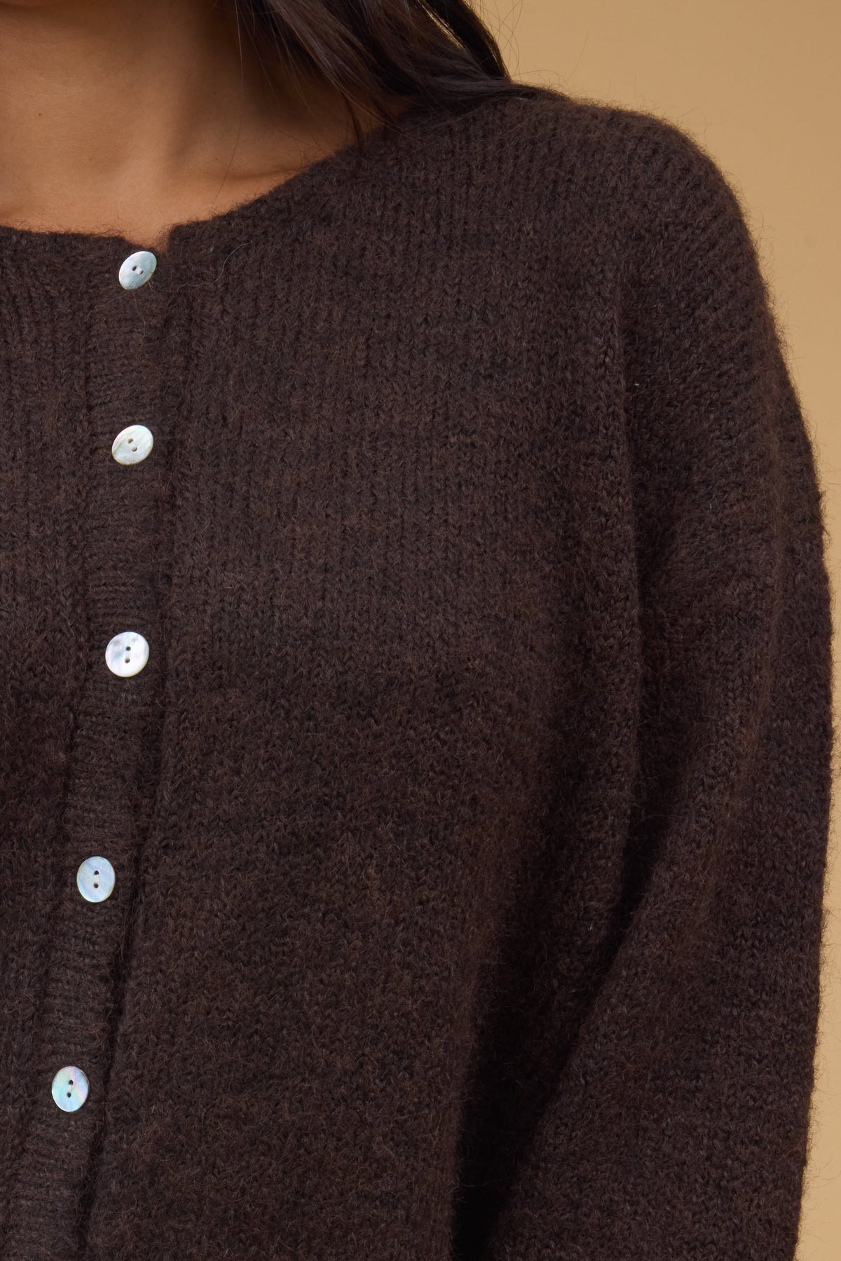 Close view of a woman wearing a brown rib knit cardigan with a round neckline and long sleeves.