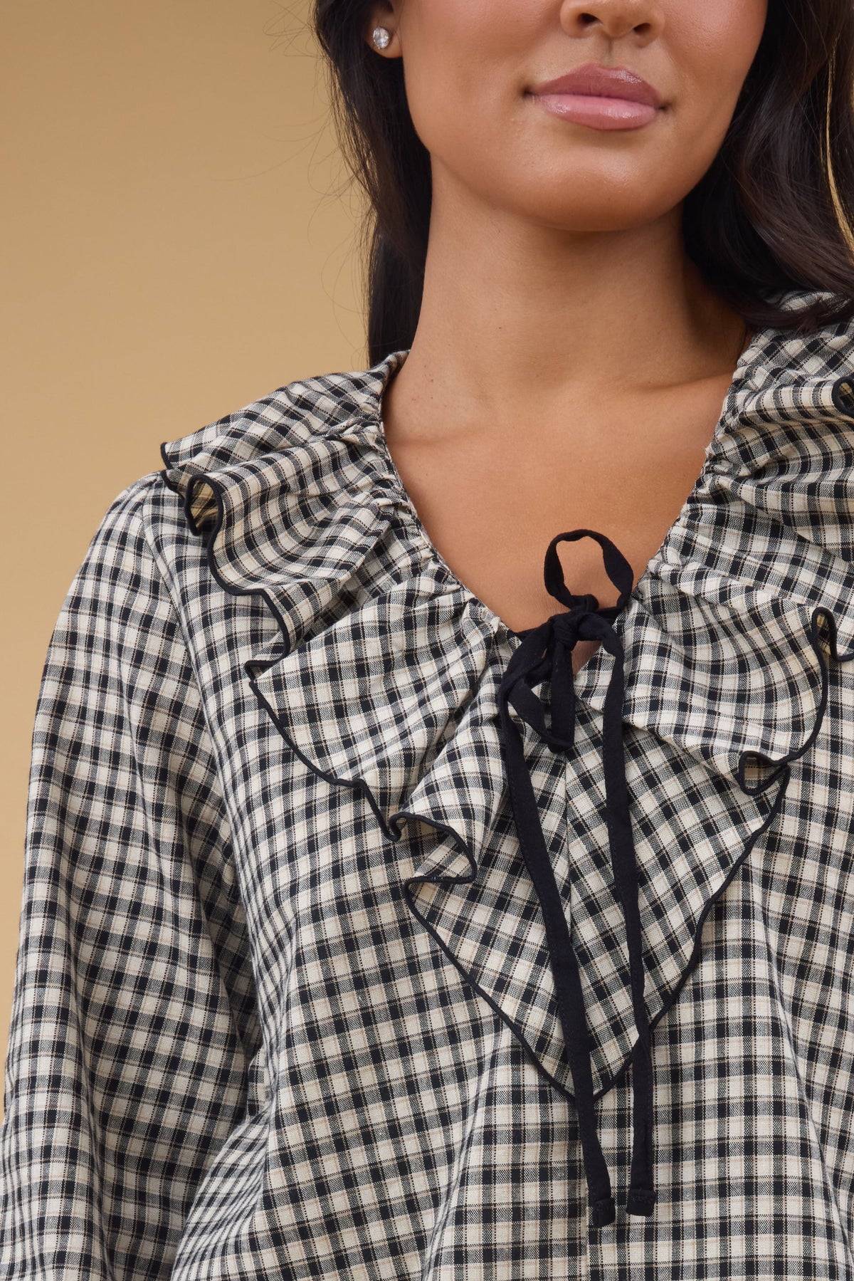 Close view of a young woman wearing a plaid & tan blouse with a ruffled V-neckline and a string bow at the bottom of the neckline.
