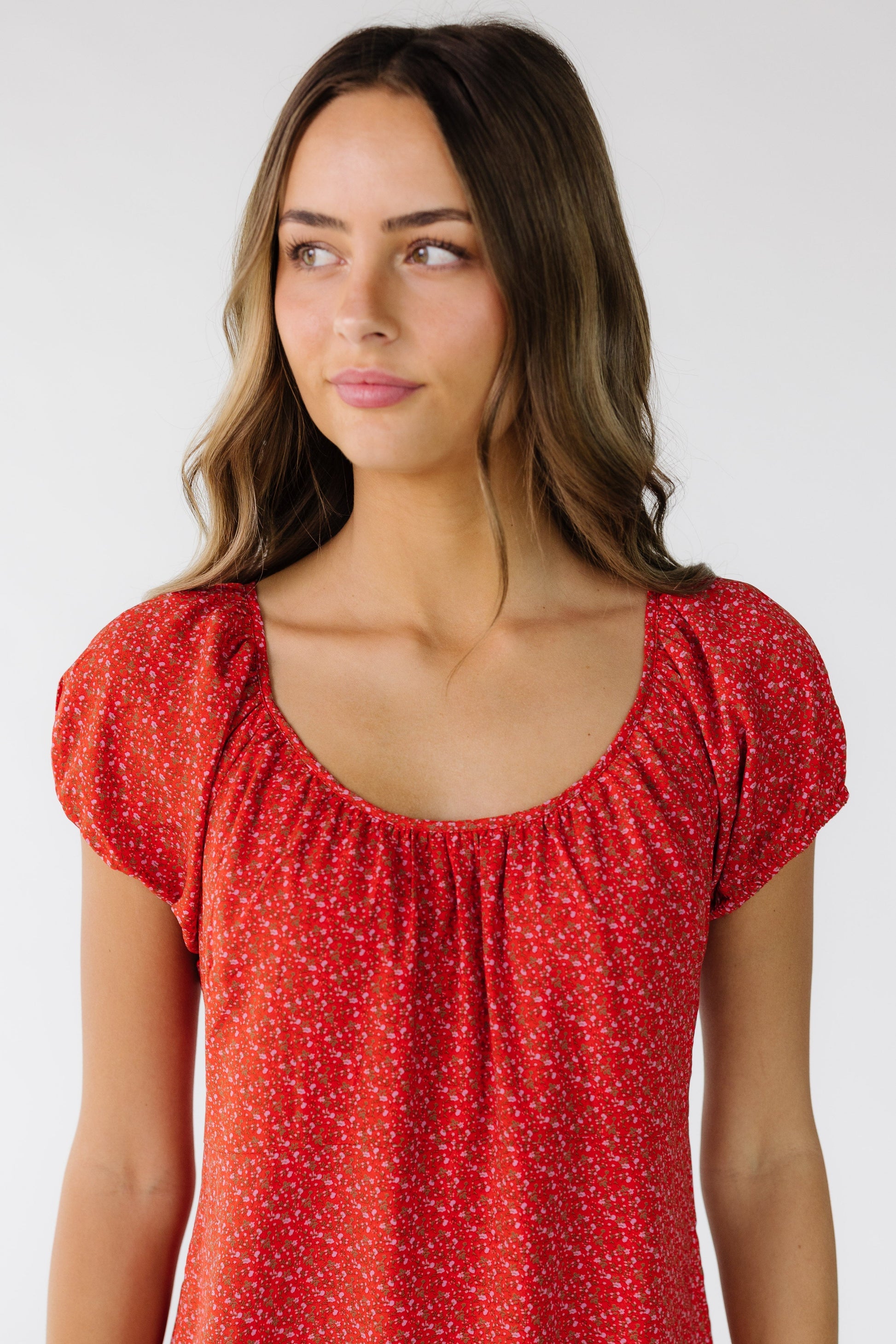 Close view of a young woman wearing a red floral print dress with a scoop neckline and short puff sleeves.