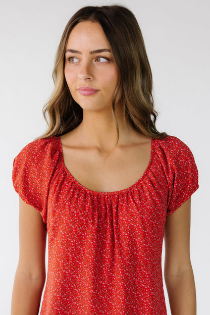 Close view of a young woman wearing a red floral print dress with a scoop neckline and short puff sleeves.