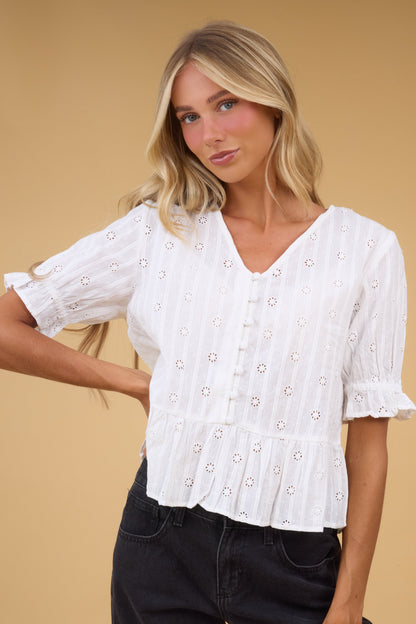 Young woman wearing a loose fitting white eyelet blouse with a V-neckline and short sleeves.