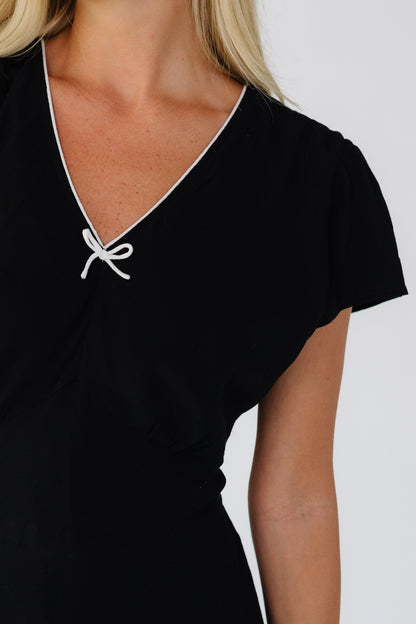 Close view of a young woman wearing a black dress with short sleeves, and a V-neckline with white trim.