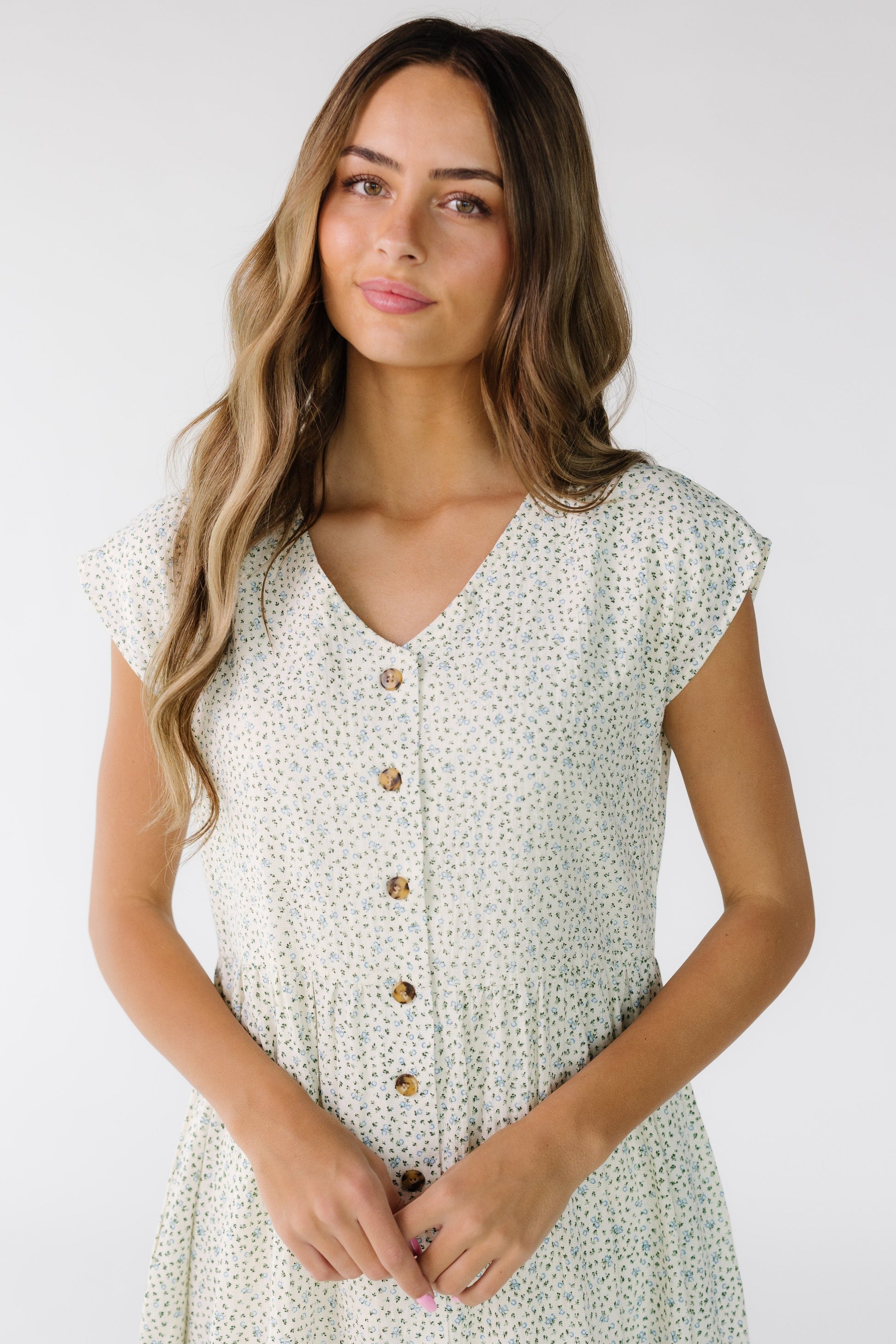 Close view  of a young woman wearing a white floral print, button down dress with short sleeves and a V-neckline.
