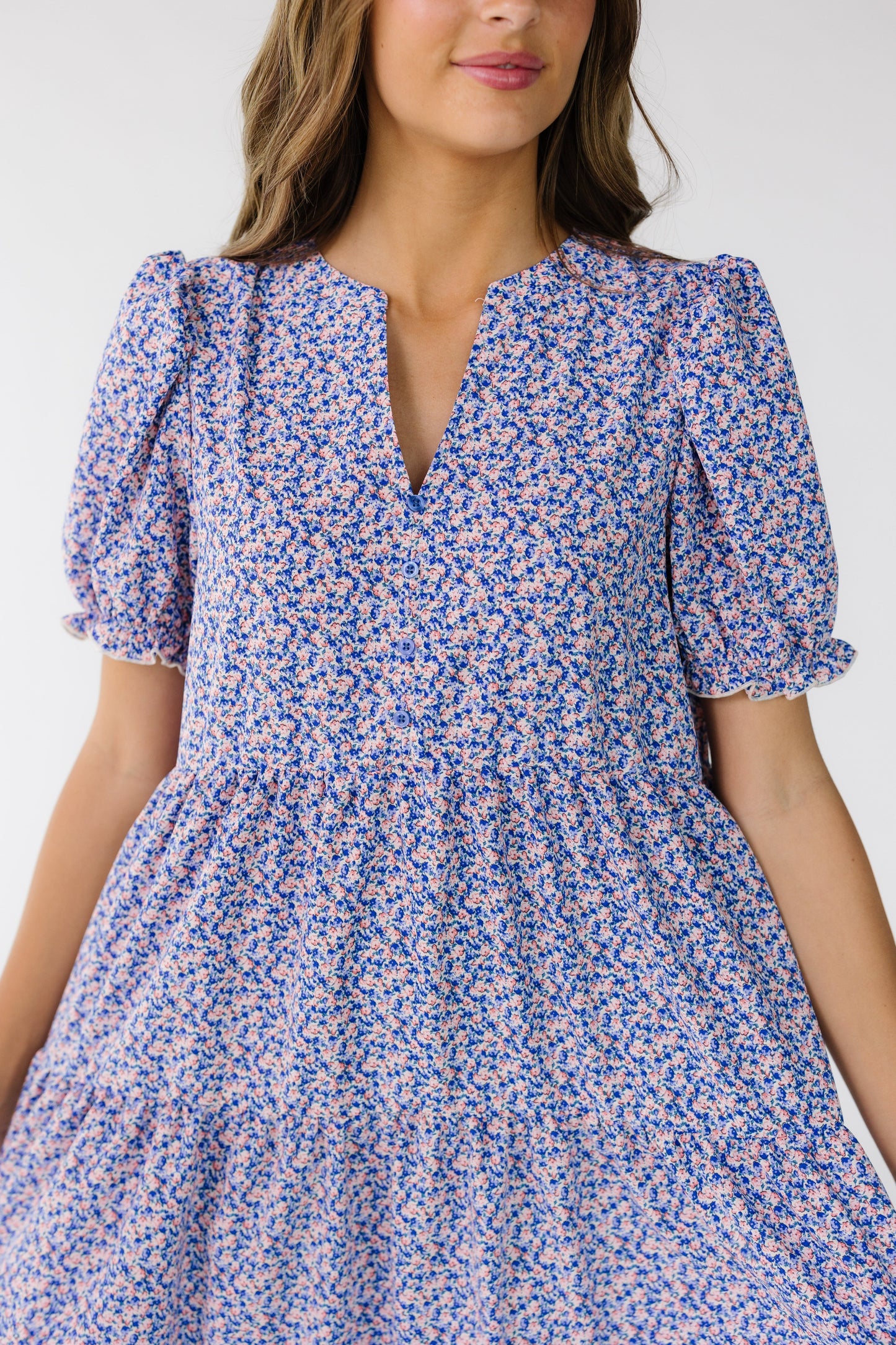 Close mid view of a woman wearing a loose fitting purple floral print dress with a V-neckline and short puff sleeves.