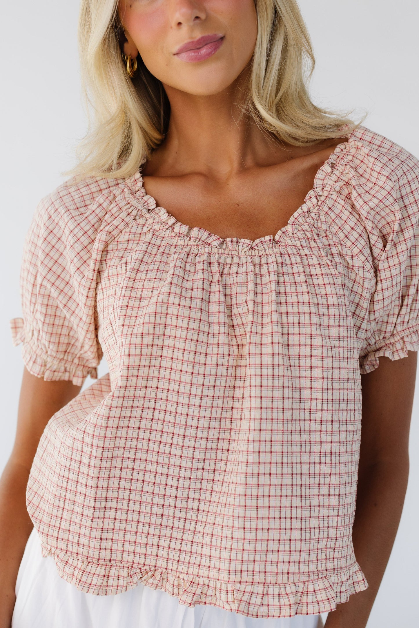 Close up view of a woman wearing a red plaid, loose fitting blouse with an elastic scoop neckline and short puff sleeves.