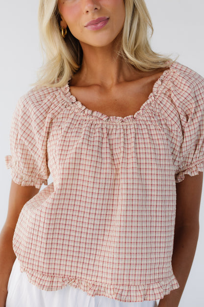 Close up view of a woman wearing a red plaid, loose fitting blouse with an elastic scoop neckline and short puff sleeves.
