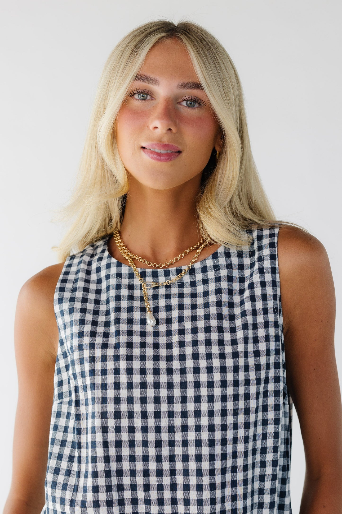 Close view of a woman wearing a blue gingham sleeveless dress with a round neckline.