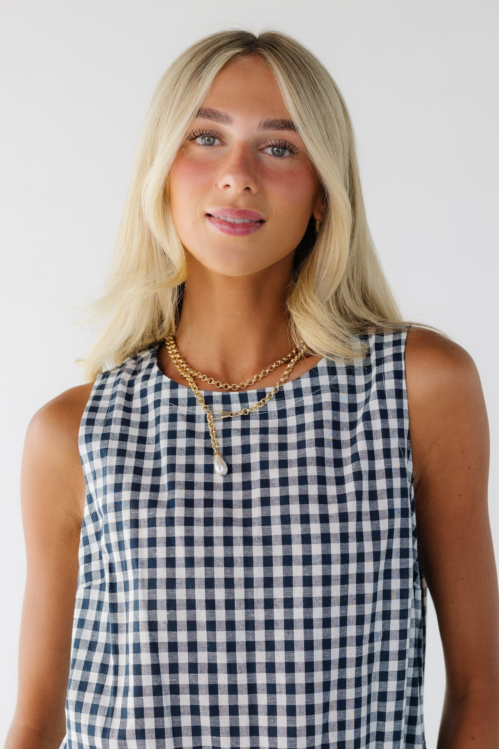 Close view of a woman wearing a blue gingham sleeveless dress with a round neckline.