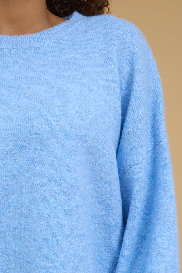 Close view of a teenage girl wearing a light blue loose fitting pullover sweater witha crew neckline, drop shoulders and long sleeves.