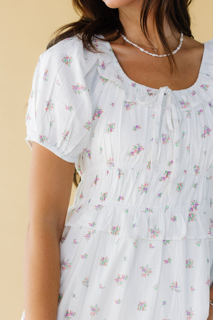 Close view of a woman wearing a white with pink & lavender floral print with a scoop neckline and puff sleeves.