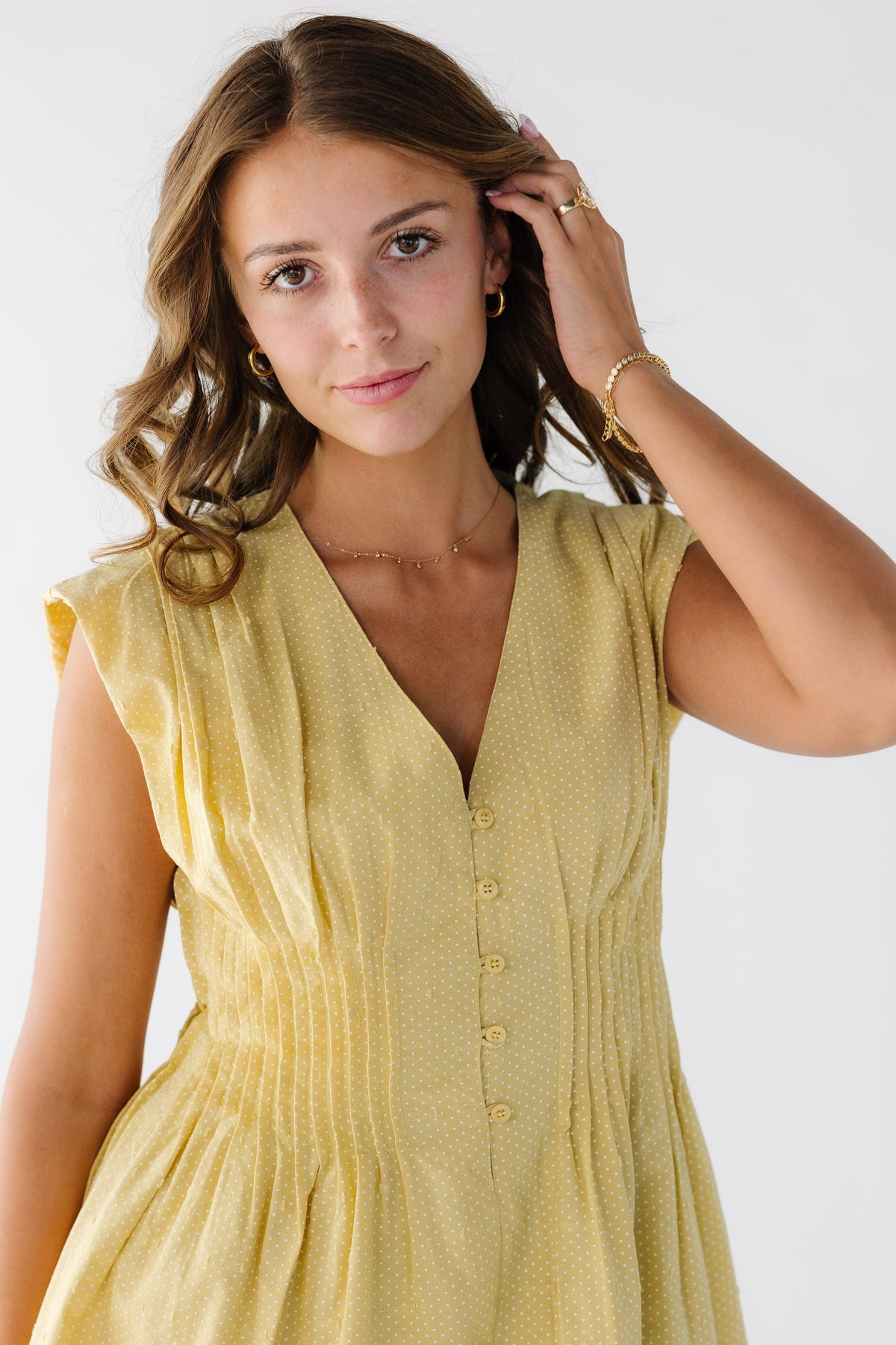 Close view of a young woman wearing a yellow sleeveless dress with tiny polka dots and pleats around the waist creating an  hourglass silhouette.