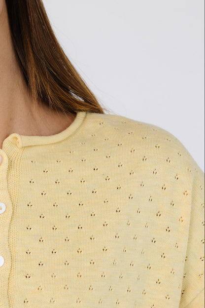 Close view of a woman wearing a light yellow pointelle knit button down cardigan.