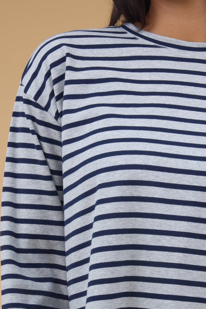 Close view of a woman wearing a grey & navy stripe, long sleeve tee with long sleeves and a round neckline.
