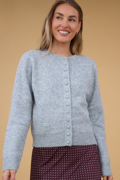 Young woman wearing a modest long sleeve cardigan in light grey with a round neckline and matching covered buttons.
