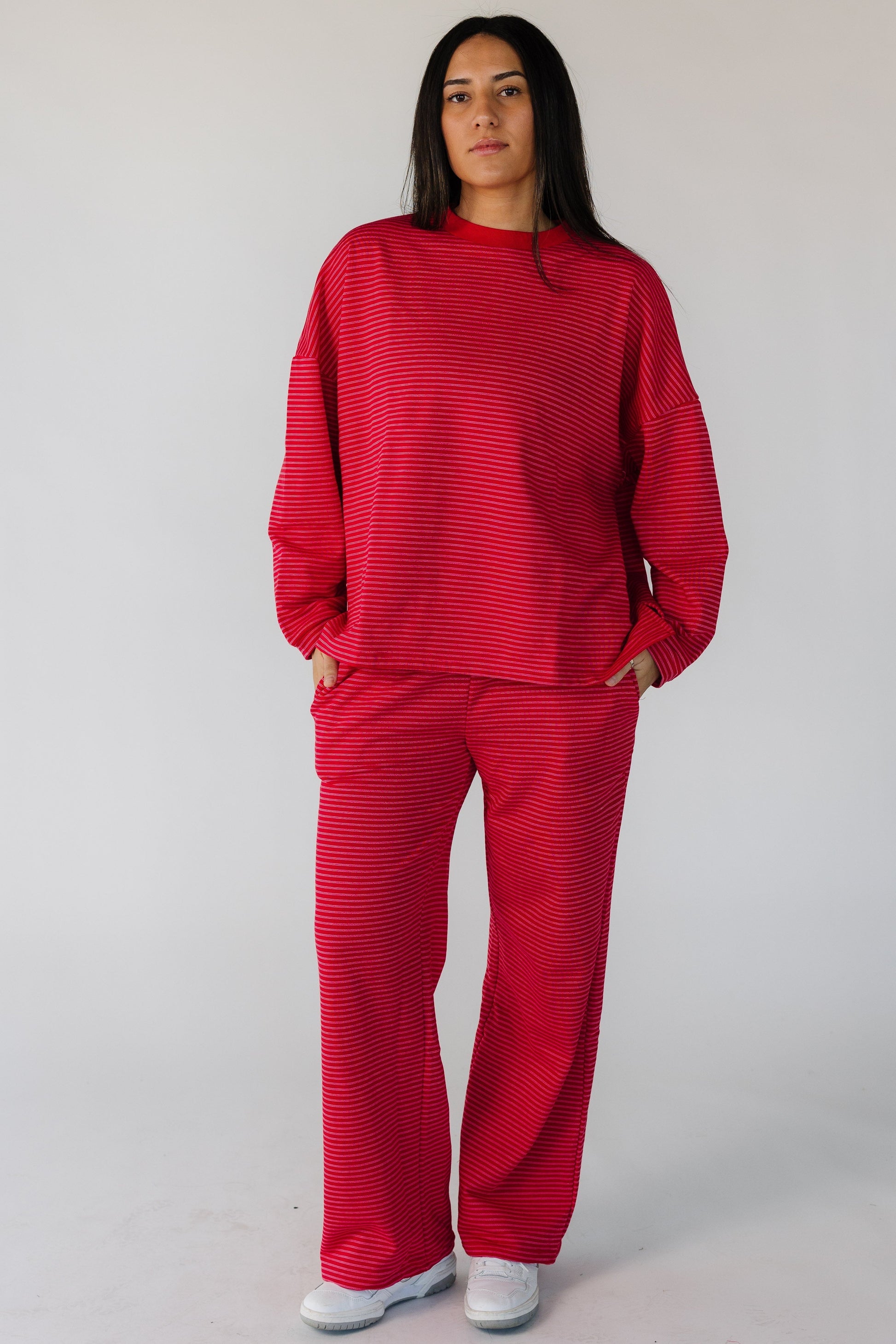 Woman wearing a red terry lounge set with double white stripes with long sleeves and long pants with side pockets.