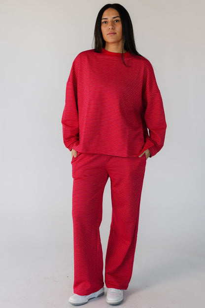 Woman wearing a red terry lounge set with double white stripes with long sleeves and long pants with side pockets.