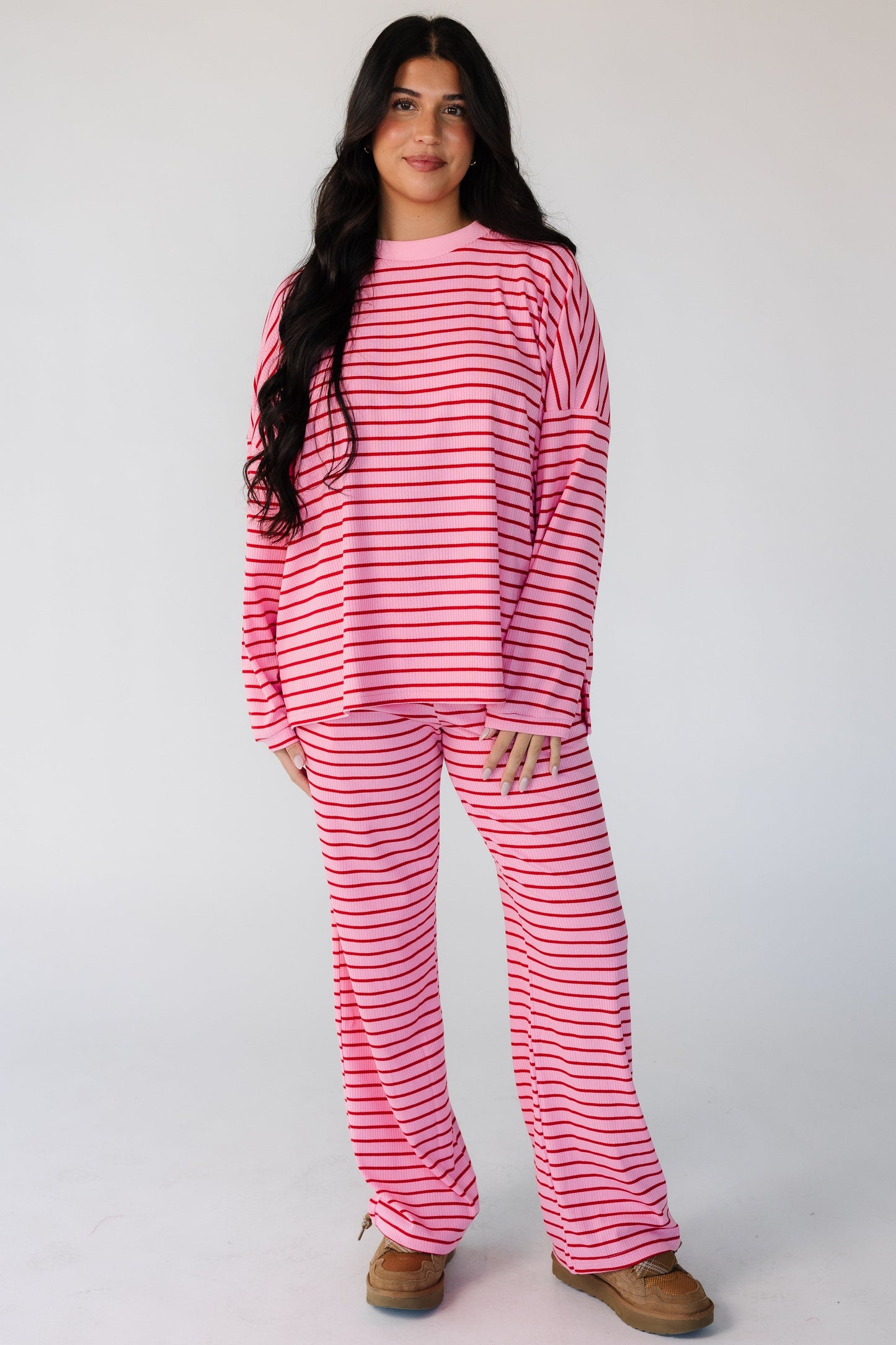 Woman wearing a modest 2 piece ribbed lounge set in pink with red stripes and long sleeves ad long pants.