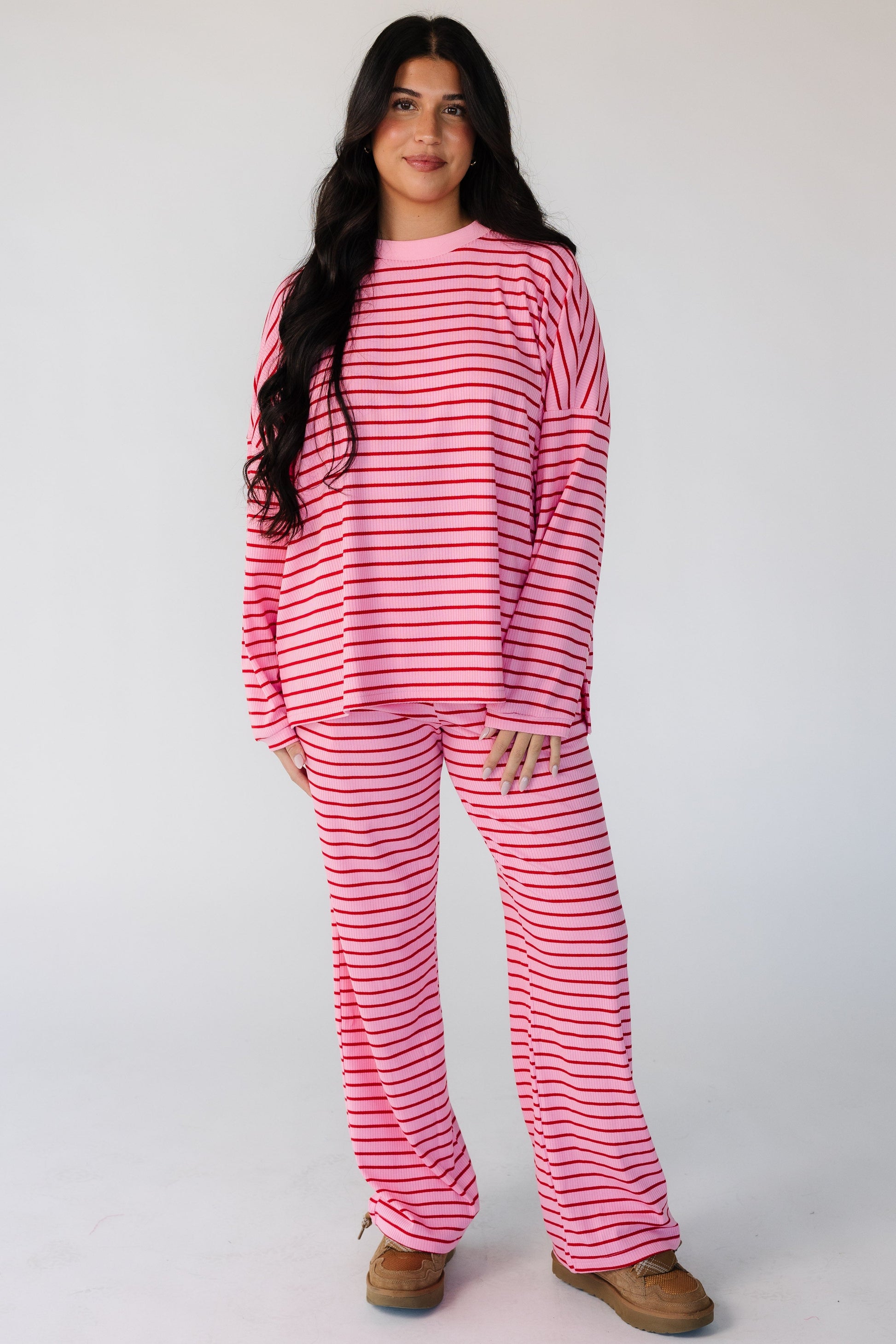 Woman wearing a modest 2 piece ribbed lounge set in pink with red stripes and long sleeves ad long pants.