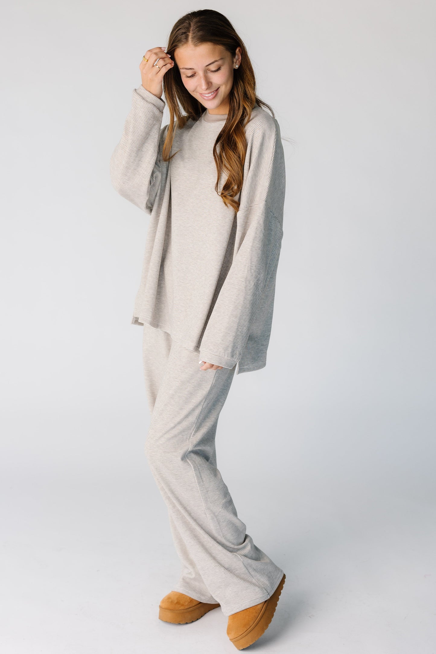 Woman wearing a loose fitting 2 piece lounge set with a crew neckline and side pants pockets.