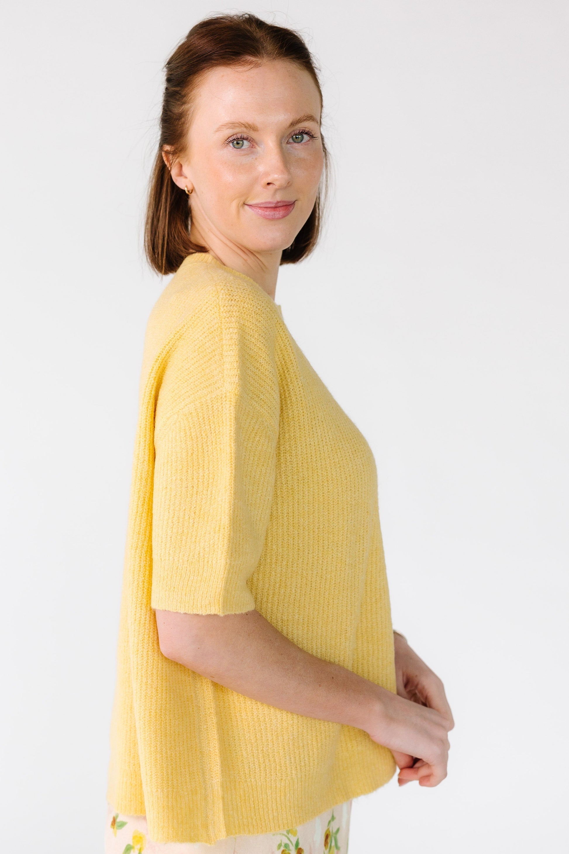 Side view of a woman wearing a yellow rib knit cardigan with short sleeves.