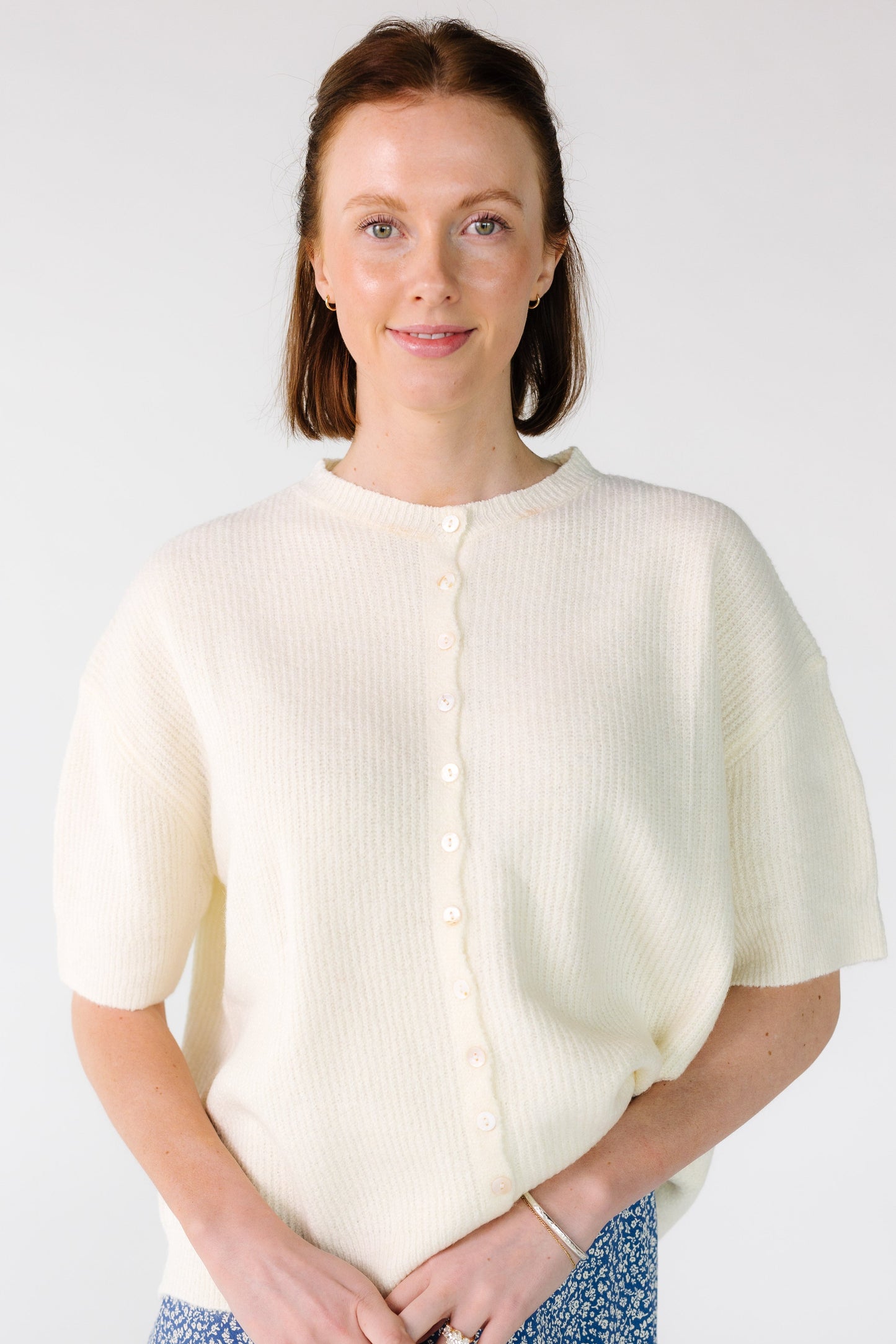 Woman wearing an ivory button down cardigan with short sleeves.