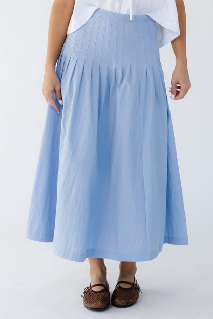 Woman wearing a blue midi skirt with sewn down pleats all around the hip.