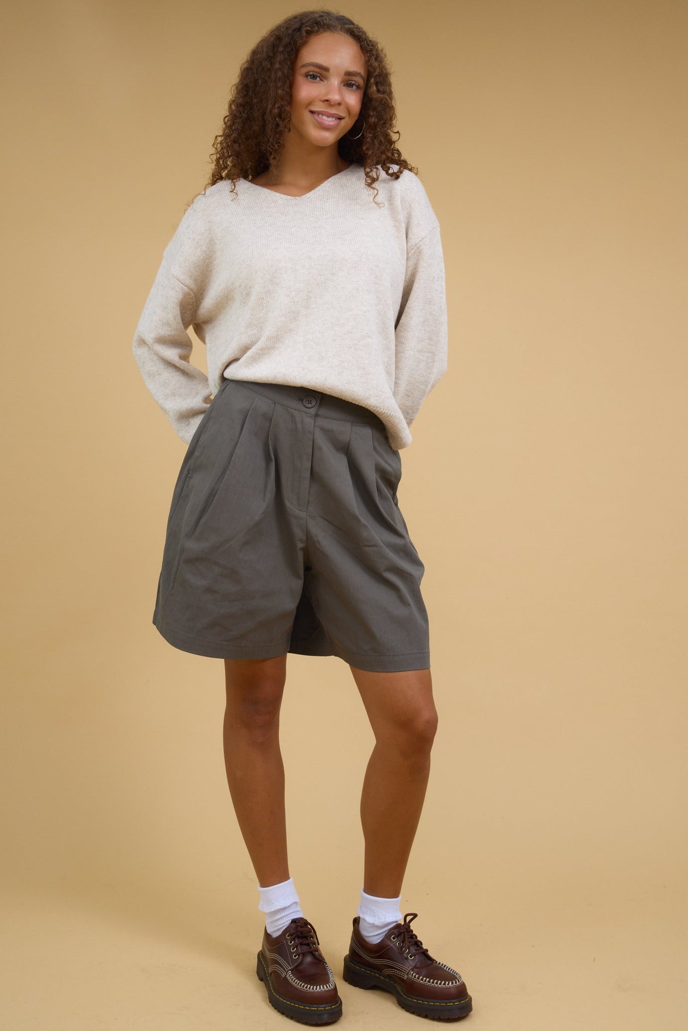 Teenage girl wearing olive trouser shorts with front pleats and side pockets.
