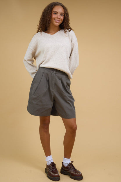 Teenage girl wearing olive trouser shorts with front pleats and side pockets.