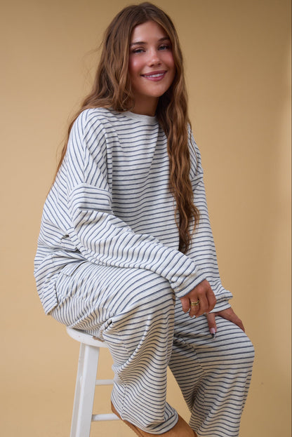 Young woman wearing a light grey stripe lounge set with long sleeves and wide long pnat legs.