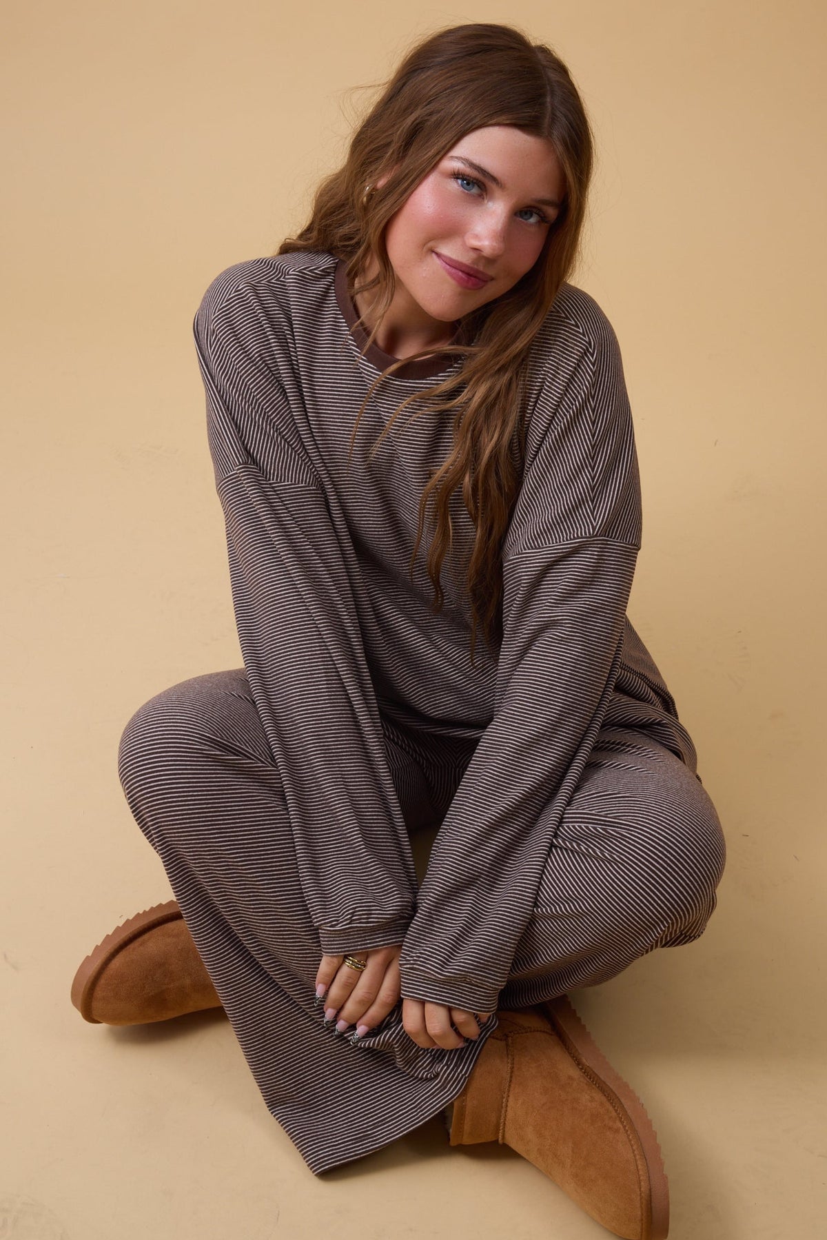 Young woman wearing a brown stripe loose fitting lounge set with long sleeves and wide, long pant legs.