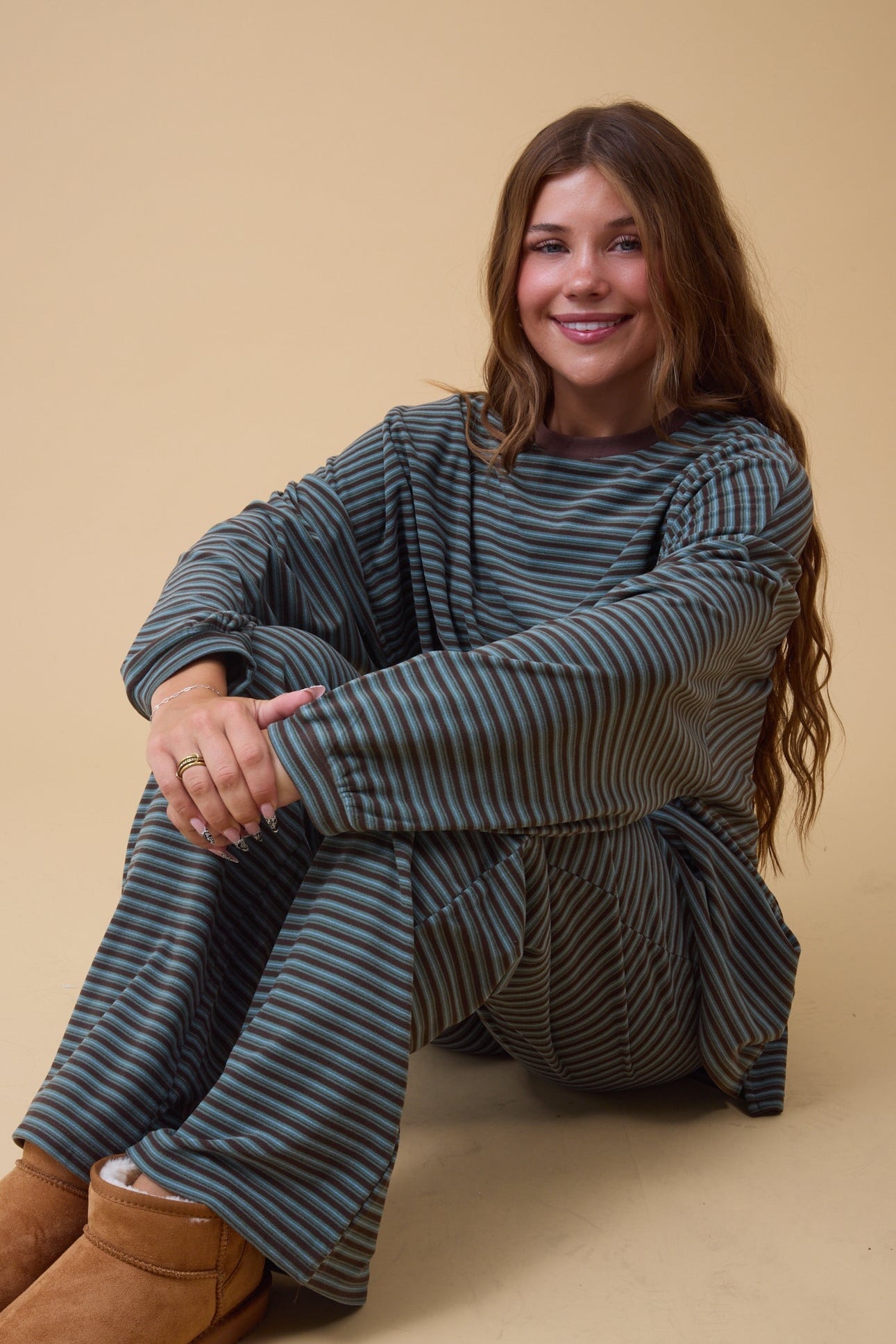 Young woman wearing a teal & brown stripe lounge set with long sleeves and long wide pants.
