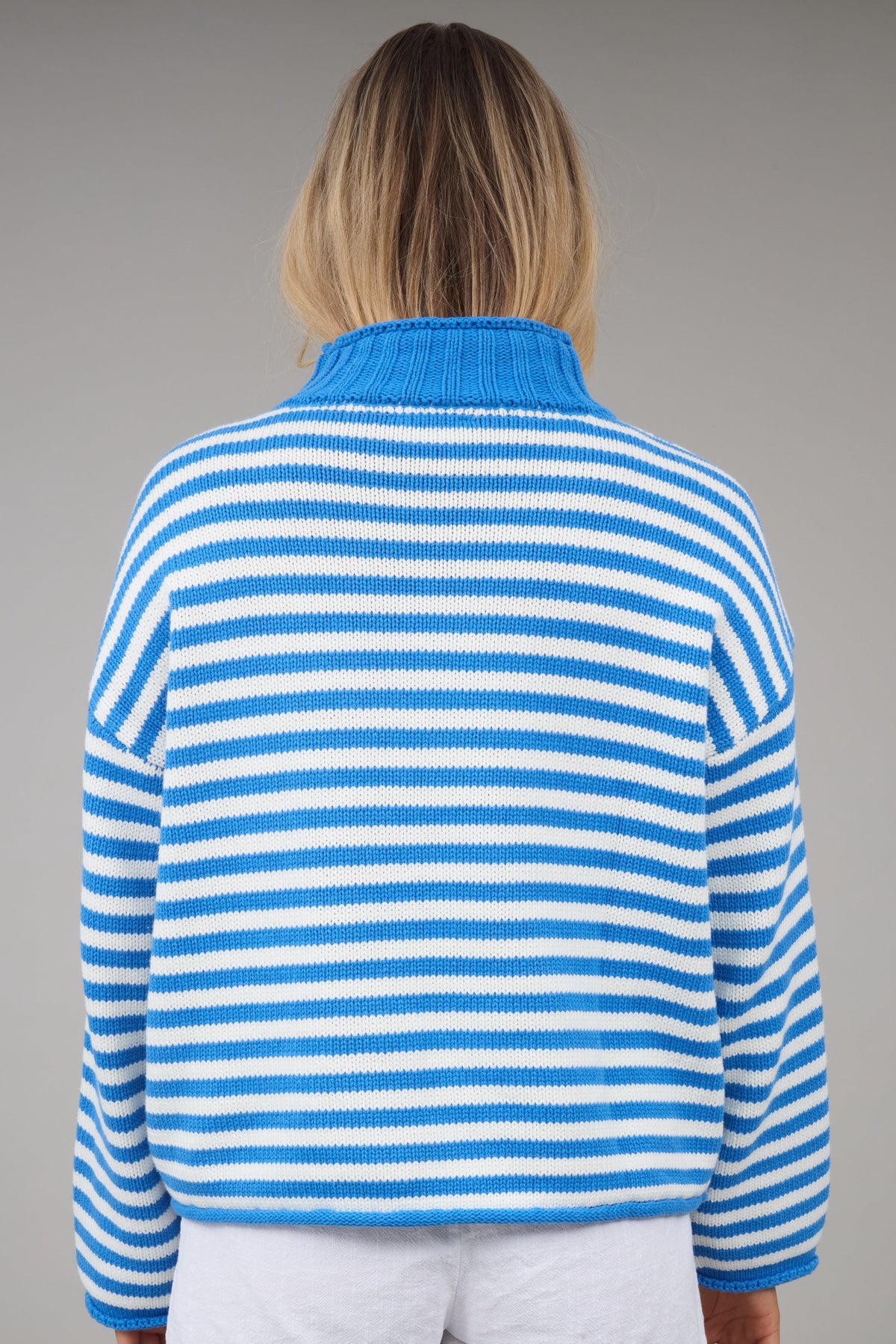 Back view of a woman wearing a loose fitting blue & white stripe sweater.