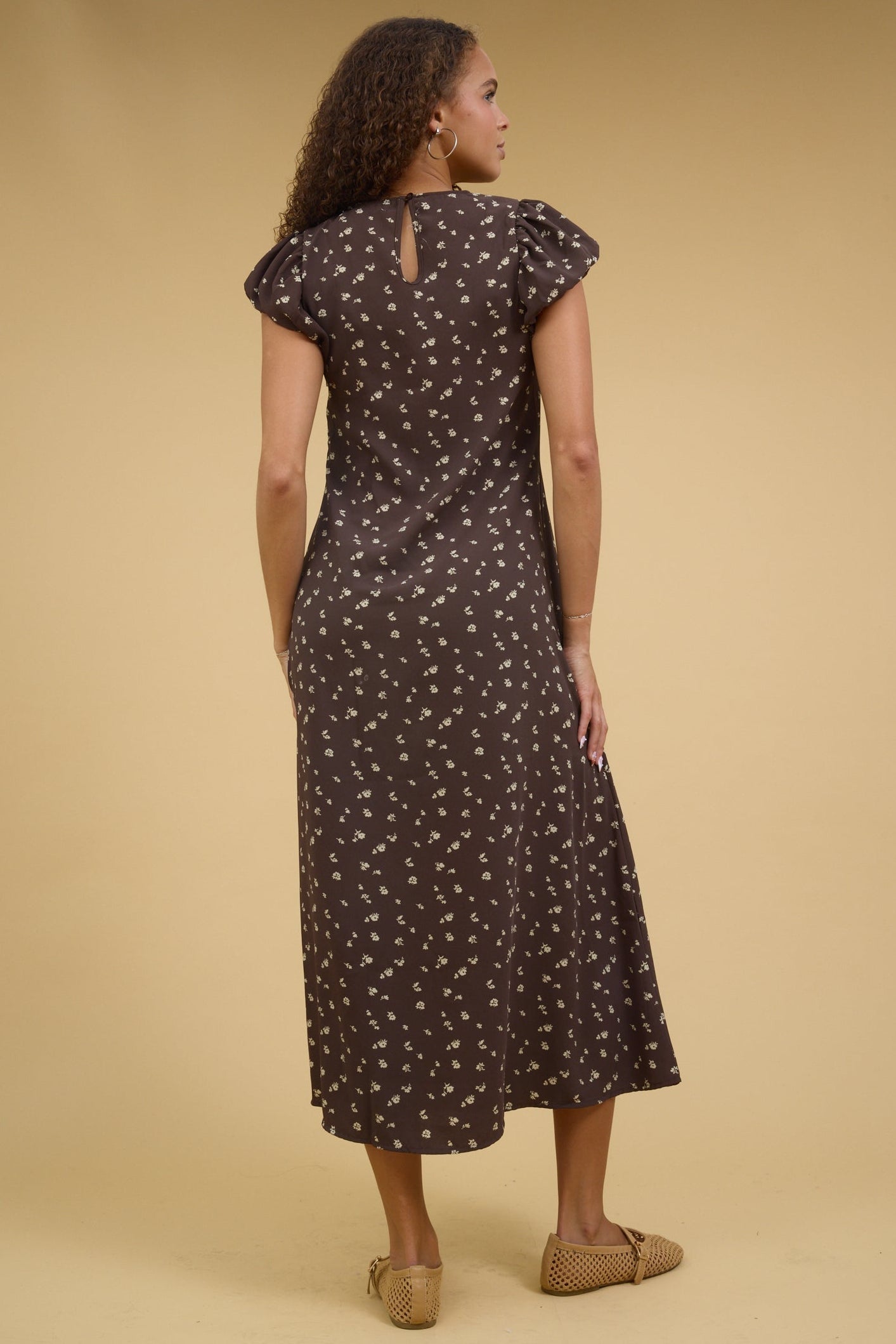 Back view of a young woman wearing a brown floral midi dress with gathered cap sleeves.