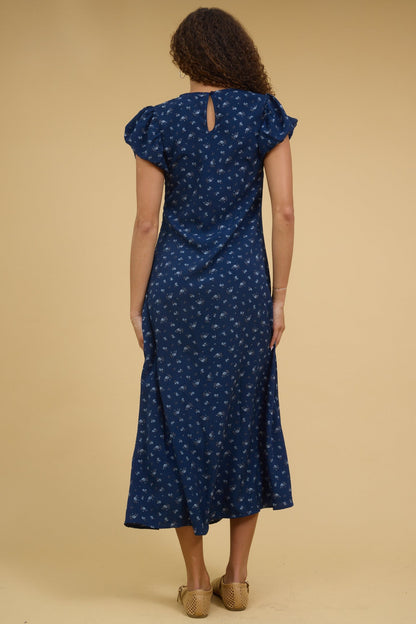 Back view of a young woman wearing a blue floral midi dress with gathered cap sleeves.