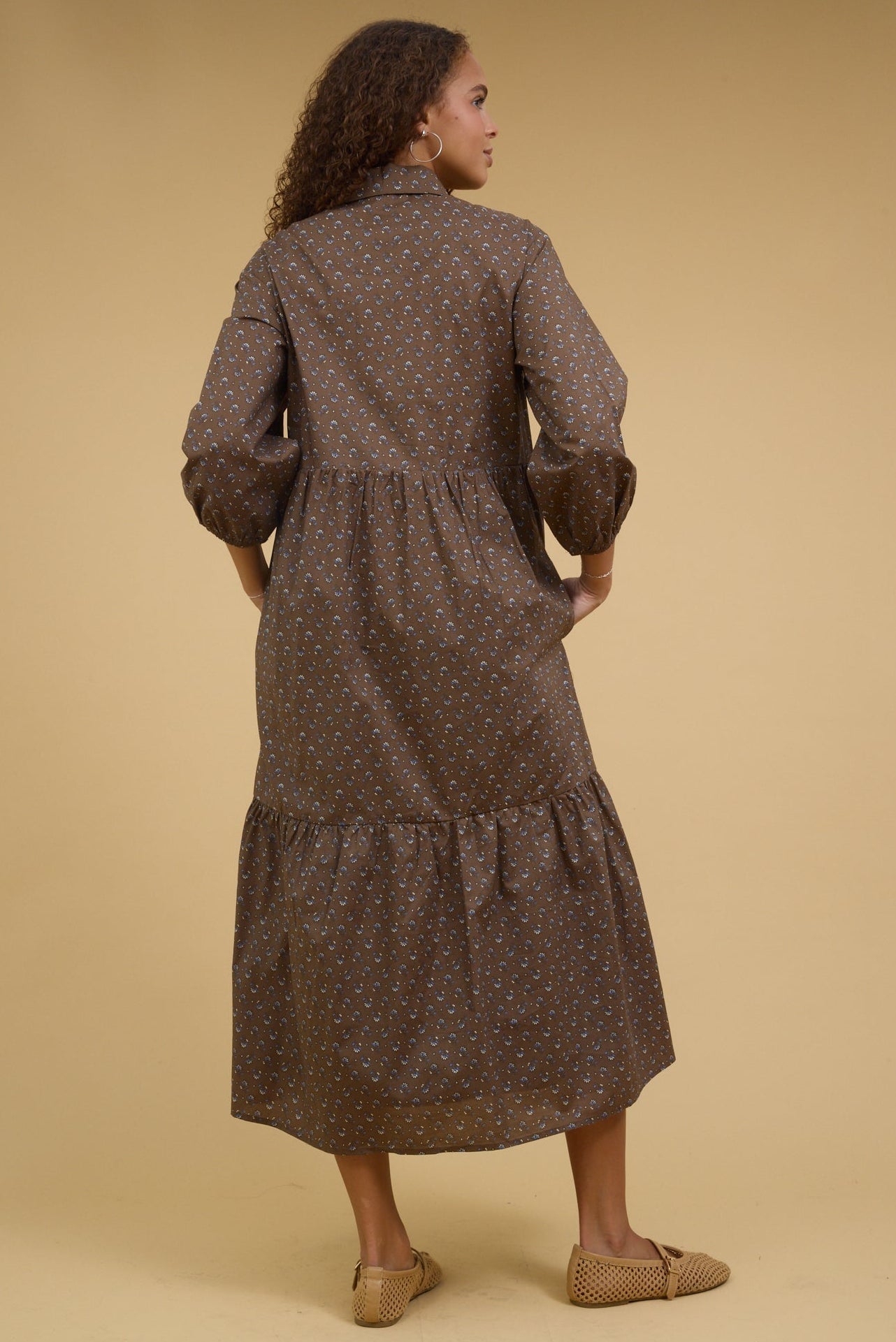 Back view of a teenage girl wearing a brown print midi dress with long sleeves.